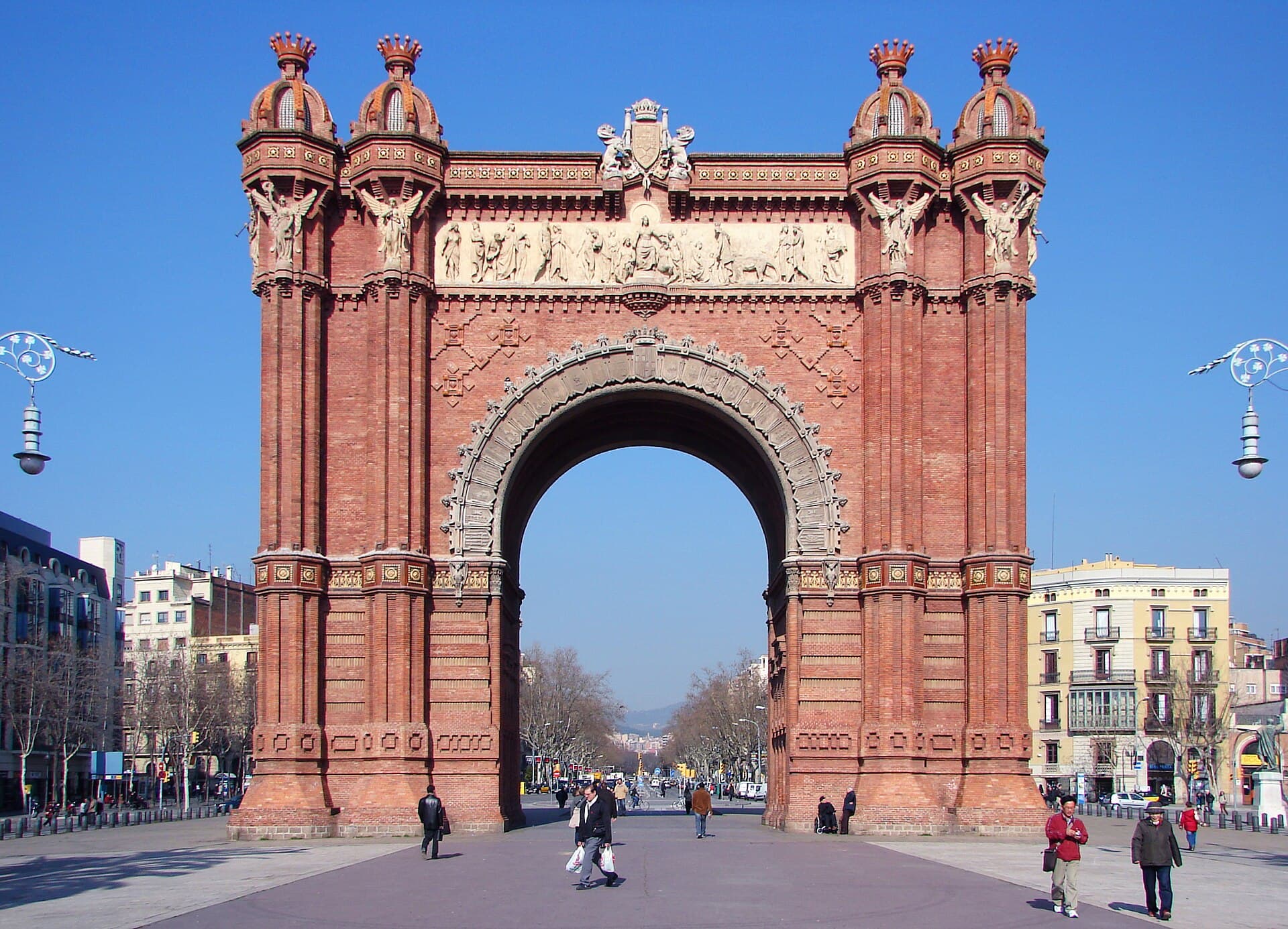 L'Arc de Triomf de Barcelone en brique rouge sous un ciel bleu, au début du passeig de Lluís Companys bordé de palmiers