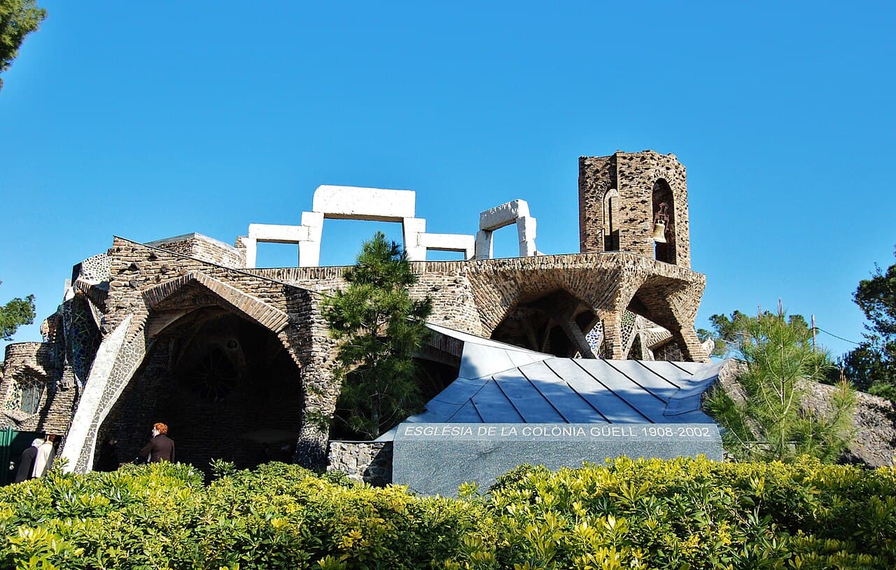 L'extérieur de la crypte Gaudí de la Colònia Güell à Santa Coloma de Cervelló, avec ses arcs de brique inclinés, son porche en forme d'auvent et son clocher surmonté d'une cloche